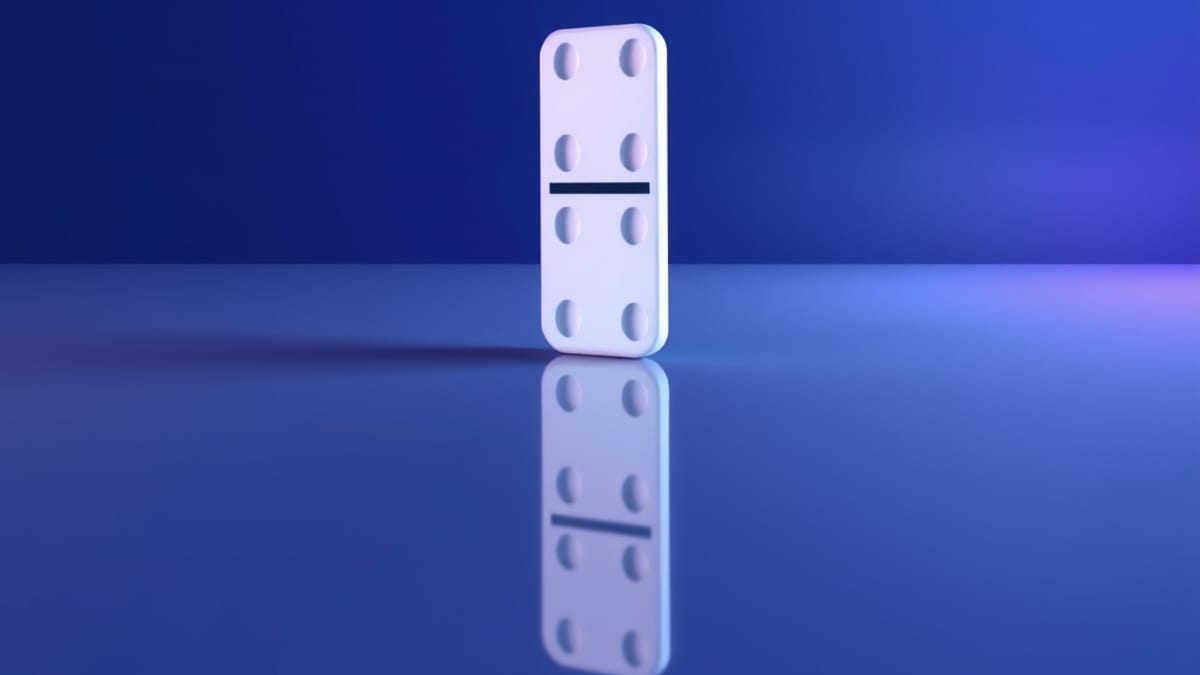 One upright domino above a mirror that reflects a differently angled domino, on a pale grey floor.