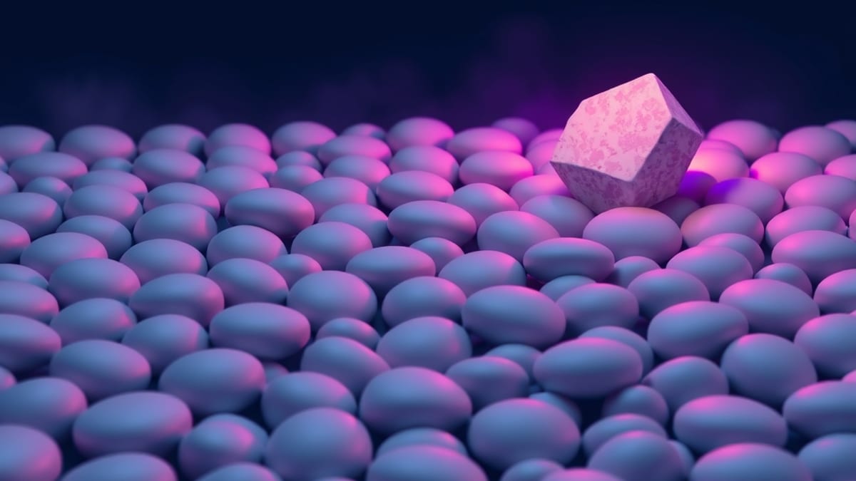 A grey fog of rounded blobs covers rows of identical smooth pebbles, with one sharply faceted, warm-lit stone standing clear 